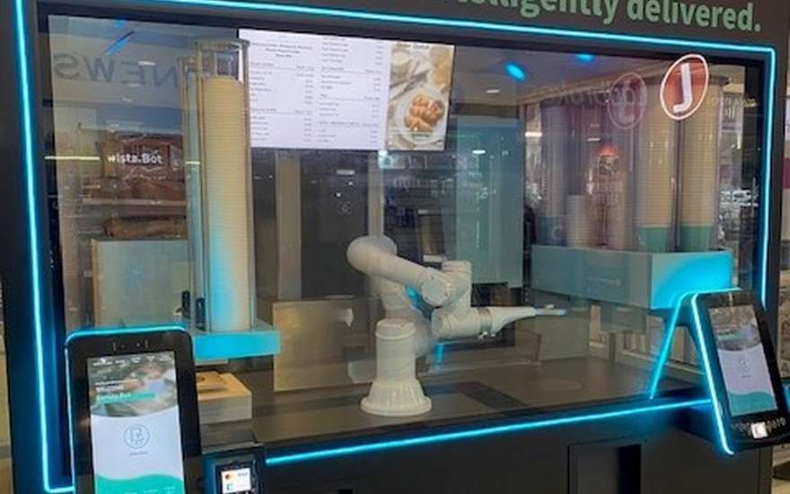 Barista.Bot kiosk lit in cyan with the robotic arm poised over a cup